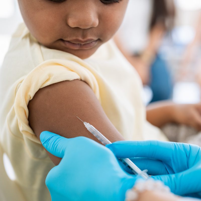 Immunisation. Protecting children from diseases. Close-up nurse in medical gloves giving injection to little patient. Brave boy getting a flu shot at doctor's office and looking at needle